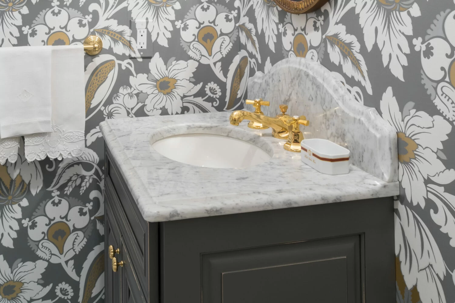 A small, dark gray bathroom vanity with a single sink against a bold wallpaper in a small bathroom
