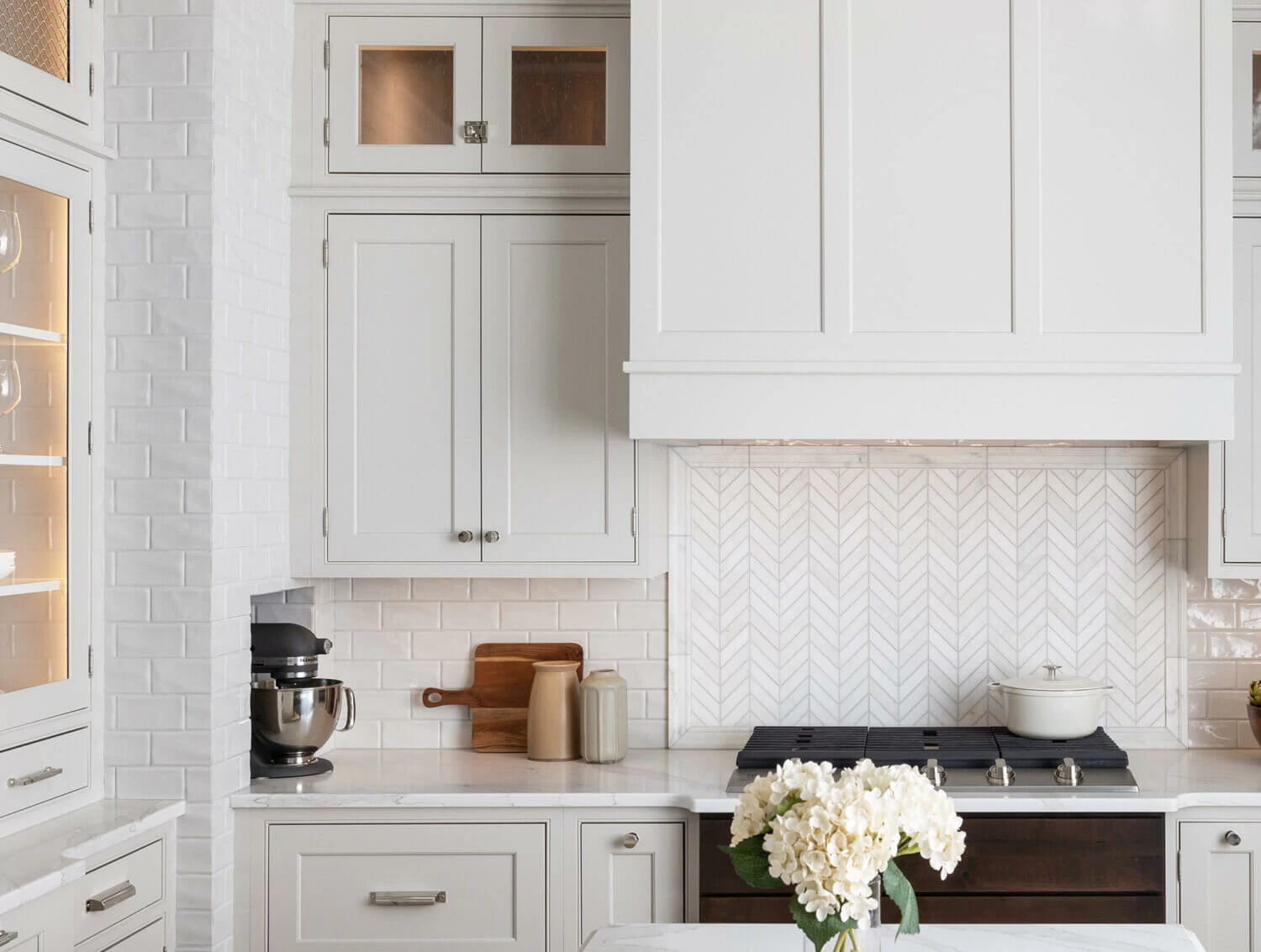 a white kitchen with beige accents in the backsplash, beautifully styled kitchen